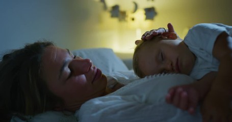 Authentic cinematic shot of young peaceful neo mother is cuddling her newborn baby while sleeping on bed in nursery at night. Concept:sweet dreams,childhood, life, maternity, motherhood, authenticity - Powered by Adobe