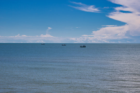 This unique photo shows three fishing boats floating in the pacific ocean in calm seas and blue skies with white clouds.