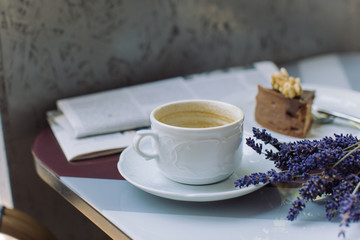Close up of cup of coffee, lavender bouquet, cream dessert, newspaper on table. Morning coffee breakfast.