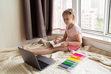 Little child learn english online at home. Homeschooling and distance education for kids. Caucasian Girl student drawing english letters at the notebook during coronavirus covid-19 quarantine