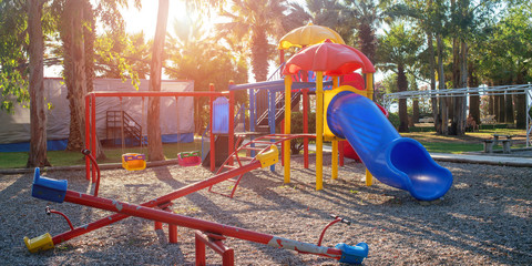 children playground with colorful swing and plastic slide on sand in public park