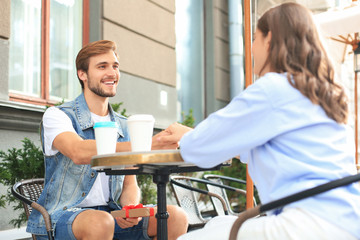 Obraz premium Smiling young girl having a date with her boyfriend at the coffee shop, man holding present box.