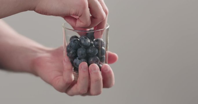 Slow motion man hands take wet washed ripe blueberries from glass jar on neutral background
