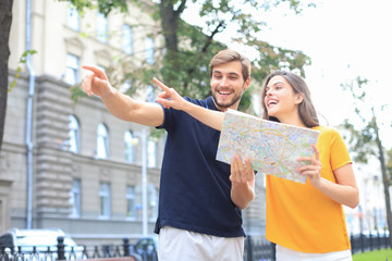 Naklejka premium Beautiful young couple holding a map and smiling while standing outdoors.