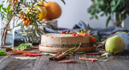 Brown mousse cake decorated with autumn leaves and berries. Wooden background. Concept of autumn mood and atmosphere