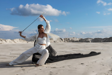 Attractive woman with sword in total white outfit. Fashion shoot in desert
