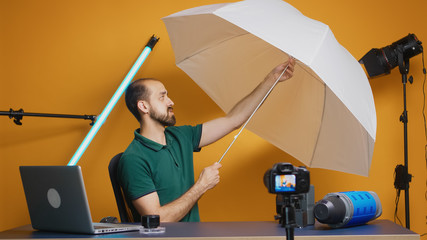 Photographer holding white umbrella for strobe in studio while recording vlog. Professional studio...