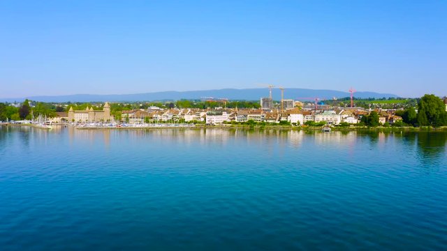Calm Water Of Lake Leman With Boats Moored On The Harbor Revealing The Beautiful City Of Morges In Vaud, Switzerland - aerial drone (climb - tilt-down shot)