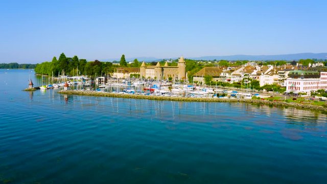 Boats Anchored On The Harbor By The Lake Leman With Morges Town And Castle On The Lakeshore In The Canton Of Vaud In Switzerland - low aerial drone