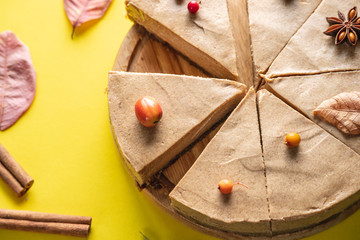 Brown mousse cake minimally decorated with autumn symbols on a yellow background. Concept of seasons and autumn mood