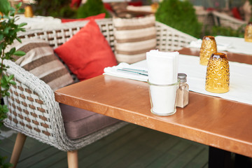 Summer terrace veranda of the cafe. Cozy gray wicker chairs with cushions, served tables and green bushes