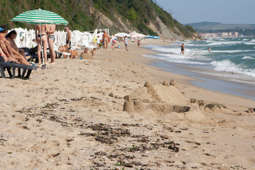 A beach with holidaymakers on the black sea and a sand castle in the foreground.