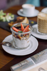 Glass jar filled with homemade granola, yogurt, fresh blueberries and strawberry served for breakfast with cup of cappuccino. Healthy eating and lifestyle concept.