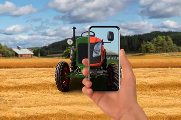 Rollo Alter Traktor auf dem Bauernhof. Darauf richtet der Bauer sein Handy und auf dem Bildschirm erscheint ein neuer moderner Traktor. © scharfsinn86