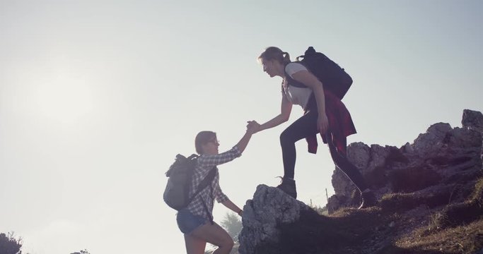 Friend help and give hand to partner to climb up summit hiking in the morning sun hike in fall or autumn sunlight flare look at the view on a local travel slowmotion