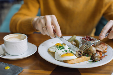 Man eating traditional English breakfast with fried eggs, sausages, beans, mushrooms, bacon at cafe in the morning.