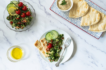 An arrangement of mezze dishes such as tabbouleh and flat breads in a top down flat lay style photo.  Plain background with copy space