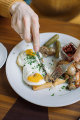Close up of plate with traditional English breakfast. Man eating fried eggs, sausages, beans, mushrooms, bacon and drinking coffee at cafe in the morning.