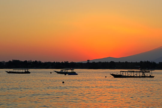 Scenic beach with boats silhouetted at sunset on a tropical island of Indonesia. © EcoView