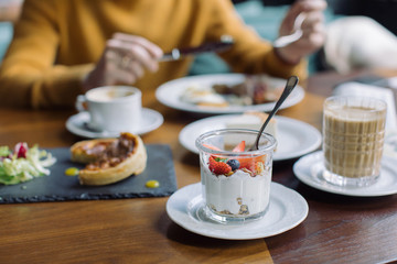Homemade granola with yogurt, cappuccino. Man eating English breakfast on background.