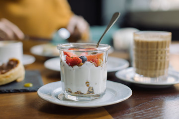 Glass jar filled with homemade granola, yogurt, fresh blueberries and strawberry served for breakfast with cup of cappuccino. Healthy eating and lifestyle concept.