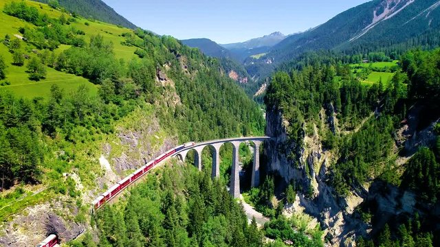 Train in the middle of a beautiful Swiss mountains. The train is heading for a bridge entering the mountain, with a beautiful landscape in background - aerial view with a drone 4K