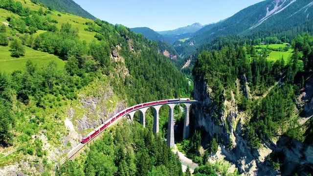 Train in the middle of a beautiful Swiss mountains. The train is heading for a bridge entering the mountain, with a beautiful landscape in background - aerial view with a drone 4K