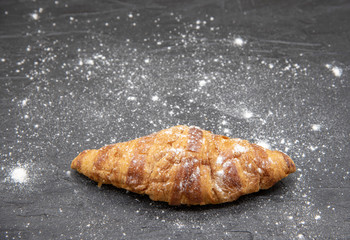 One croissant lies on a black slate background.