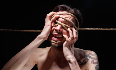 Photo of binded brunette man trying tear the rope on face