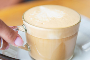 Cup of cappuccino coffee in female hands at a table in a cafe. Top view. Close-up.