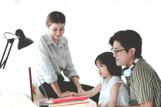 Little kid using laptop at table in room, girl studying with parents at home. Father and mother teaching daughter, happy family having fun with device and learning technology together