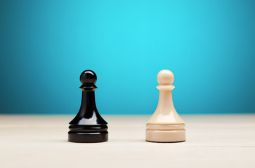 Black vs white chess pawn piece against blue background. Confrontation, competition or conflict in...