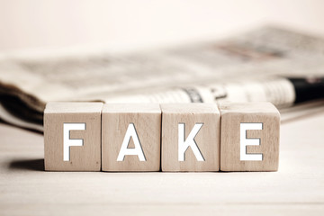 The word fake on wooden blocks against a newspaper background. Fake news in media concept.