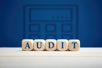 The word audit on wooden cubes with blue background with a calculator icon. Financial auditing and...