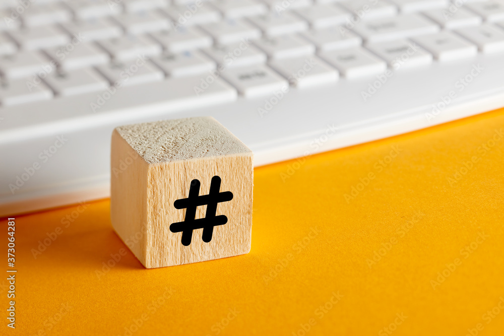 Poster hashtag symbol on a wooden cube with computer keyboard background on yellow
