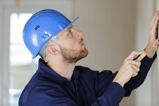 young male builder using scraper on wall