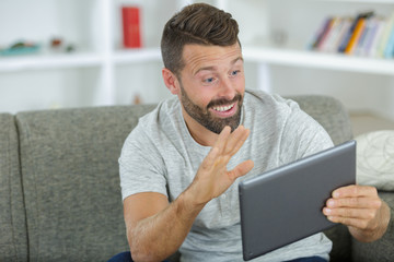 man waving hand with smiling at tablet