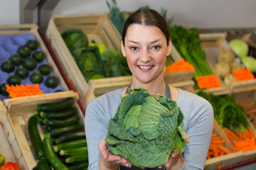 young woman seller weighing cabbage in grocery shop