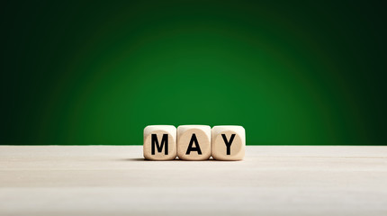 The month May written on wooden cubes against green spring background with copy space. Month of the year.