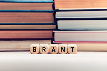 The word grant on wooden cubes with stacked books background. Education or research funding concept.