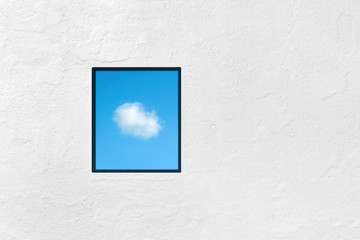 Single window on a white concrete wall with blue sky and cloud view. Imagination, dreaming, freedom or inspiration concept.