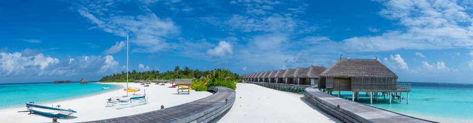 Panorama landscape of the tropical beach with over water bungalows and alms trees at the tropical island in Maldives