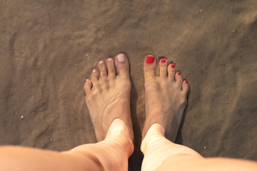 Women's feet in the water on the sand. Multi-colored pedicure