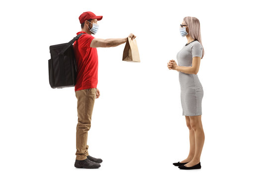 Full Length Profile Shot Of A Food Delivery Man With A Face Mask Handing A Paper Bag To A Woman