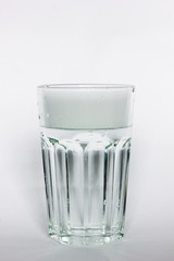 Pure drinking water in a glass cup. A stream of water and transparent droplets on the wall of the glass. Pour water on a white background.