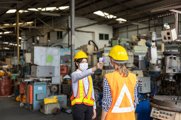 Factory in new normal. Worker uses infrared thermometer measuring temperature with  staff scanning for Coronavirus or Covid-19 symptom at factory entrance. International medical healthcare system