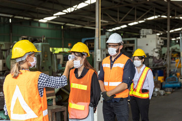 Factory in new normal. Worker uses infrared thermometer measuring temperature with  staff scanning...