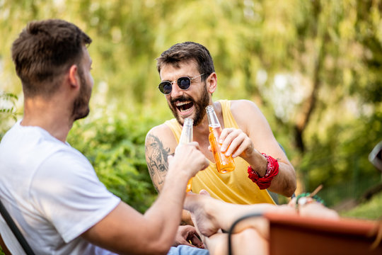 Two young men sitting, laughing, drinking beer while a young girl holds her beautiful legs between the two of them