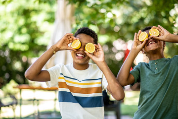 Two boys are playing with a lemon and smiling, making a lemon eye face and look at camera
