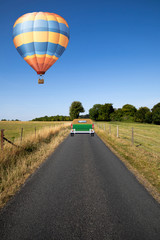 Fototapeta premium Hot air balloon flying over single lane country road through countryside and farmland